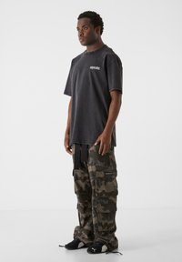 Sort oversized t-shirt med en falmet finish; camo cargo bukser med flere lommer; parret med sorte sneakers.