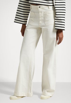 Wide-leg, cream-colored jeans made of denim, featuring five pockets, contrasting stitching, and a fitted waistband. Paired with a striped top.