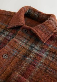 Wool plaid overshirt in warm brown with red, blue, and gray flecks. Features a collared neckline and brown buttons. Soft, textured fabric.