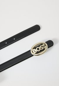 Black leather belt with a gold oval buckle featuring the word "BOSS" in capital letters. Smooth texture with adjustable holes.