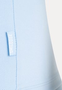 Tissu bleu clair avec un gros plan sur une couture verticale et une petite étiquette blanche en tissu lisant SMILODOX en surpiqûres bleu clair.
