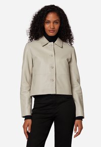 Ljust beige läderjacka i cropped-stil med krage, fem knappar och långa ärmar, matchad med en svart polotröja under.