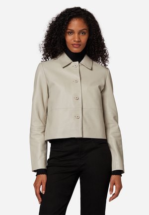 Hellbeige, aus Leder, geschnittene Jacke mit einem kragenförmigen Ausschnitt, fünf Knöpfen und langen Ärmeln, kombiniert mit einem schwarzen Rollkragenpullover darunter.