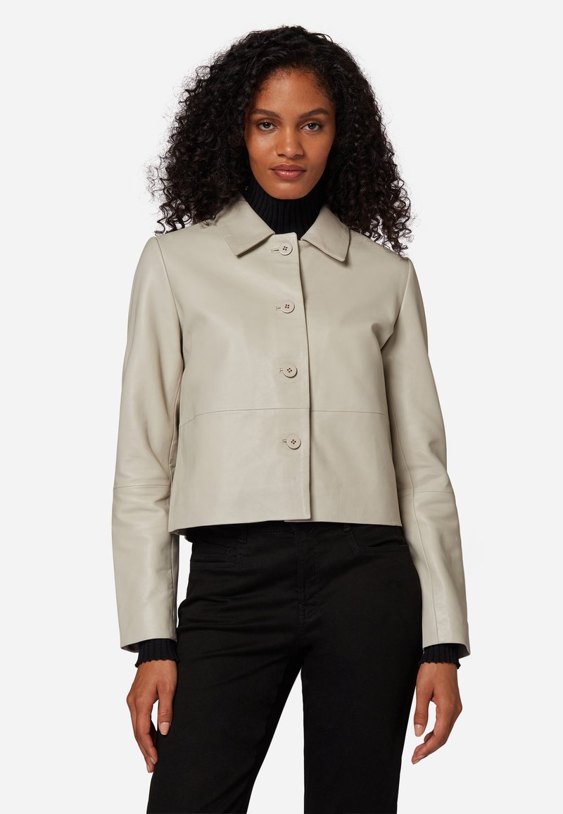 Ljust beige läderjacka i cropped-stil med krage, fem knappar och långa ärmar, matchad med en svart polotröja under.