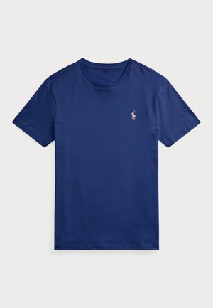 Tummansininen puuvillapaita, jossa on lyhyet hihat, pyöreä pääntie ja pieni kultaisella langalla brodeerattu logo polo-pelaajasta vasemmassa rinnassa.