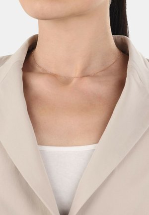 Roze gouden choker ketting met een delicate ketting en kleine ronde accenten, gedragen op een blote sleutelbeen, gecombineerd met een beige blazer.