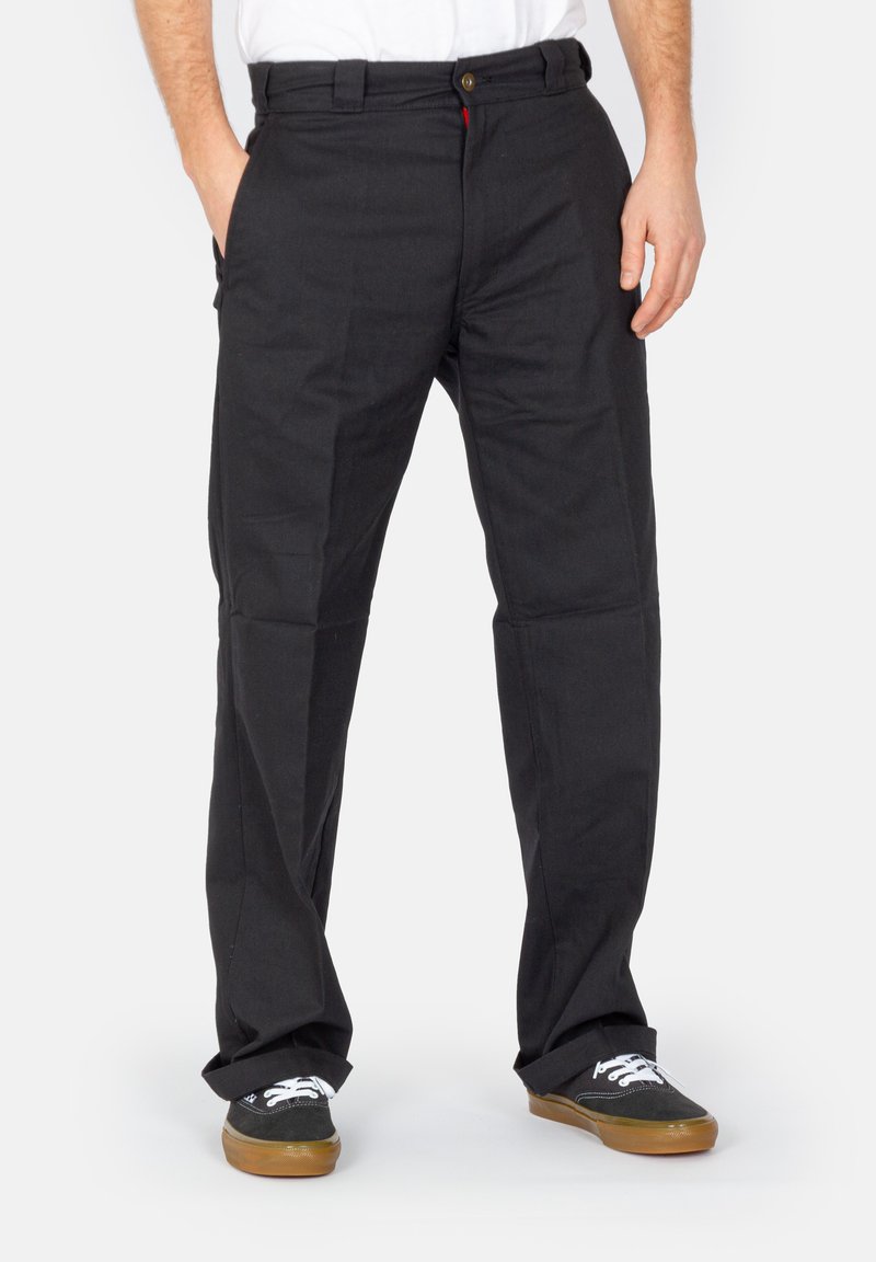 Schwarze Baumwollhose mit geradem Bein, vorderen Taschen und Knopfverschluss. Getragen mit schwarzen Sneakers mit weißen Akzenten.