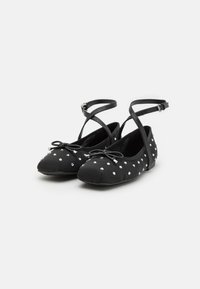 Black ballet flats with a textured fabric, featuring white polka dots, adjustable ankle straps, and a bow accent on the toe.