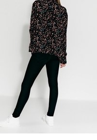 Svart blommig blus med rosa och blå mönster, parat med svarta leggings och vita sneakers. Blusen har långa ärmar och en avslappnad passform.