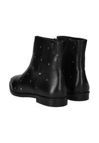 Botas de tobillo de piel negra con una textura lisa, que presentan tachuelas metálicas y una cremallera lateral. El tacón es plano con una base sólida.