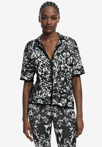 Black and white patterned short-sleeve shirt with a lapel collar and zip closure, featuring a textured fabric and contrasting black trim.