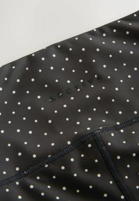 Tissu noir à pois blancs avec le texte "ACTIVE" en noir et des coutures visibles le long de la couture.