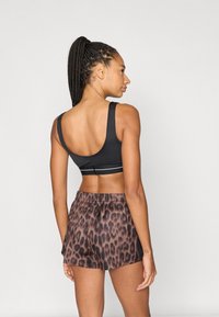Zwarte sportbeha met brede bandjes en witte accenten, gecombineerd met bruine shorts met luipaardprint. Gladde stof met elastische tailleband detail.
