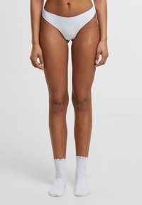 Slip da bikini bianco con un design a vita bassa e una superficie liscia. Indossato con calzini bianchi alla caviglia con bordo arricciato. Estetica pulita.