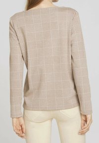 Top de manga larga a cuadros en tono beige con escote cuadrado, que presenta un tejido texturizado y un patrón de cuadrícula blanca contrastante en la parte posterior.