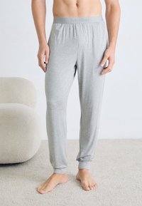 Pantaloni de pijama Calvin Klein de culoare gri deschis, cu talie elastică și picioare conice, confecționați dintr-un material moale, prezentati pe un model.