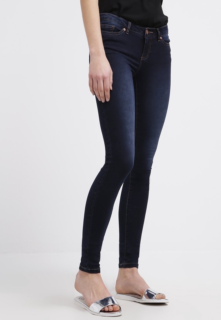 Mörkblå smala jeans med en slät textur, med en midjehöjd i medelhöjd, framfickor och subtila sömnadsdetaljer. Koppat med silverfärgade slidesandaler.