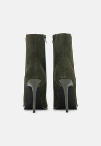 Zielone zamszowe botki za kostkę o eleganckim designie, z wąskim noskiem, wysokim obcasem typu stiletto oraz zamkami z tyłu jako detal.