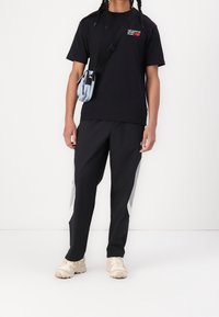 Czarny bawełniany t-shirt z czerwonym logo, czarne spodnie dresowe z szarymi paskami po bokach oraz beżowe trampki. Do tego mała jasnoniebieska torebka na ramię.