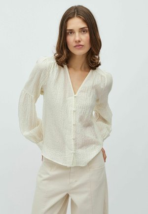 Blouse crème clair avec manches bouffantes, col en V et fermeture à boutons sur le devant. Caractérisée par un motif texturé subtil et un tissu doux et aérien.