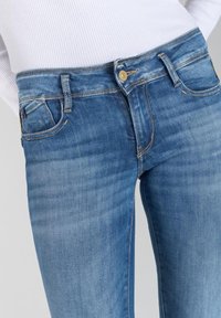 Jean en denim bleu avec une coupe mi-haute, présentant un design classique à cinq poches, une fermeture à bouton et un léger délavage pour la texture.