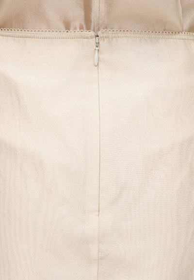 Prim-plan cu o țesătură bej, cu un fermoar alb centrat și cusături vizibile de-a lungul marginii superioare.