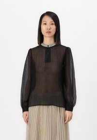 Blusa nera trasparente con lunghe maniche a sbuffo, colletto dettagliato con embellishments e apertura centrale a forma di chiave. Tessuto texture con sottili righe.