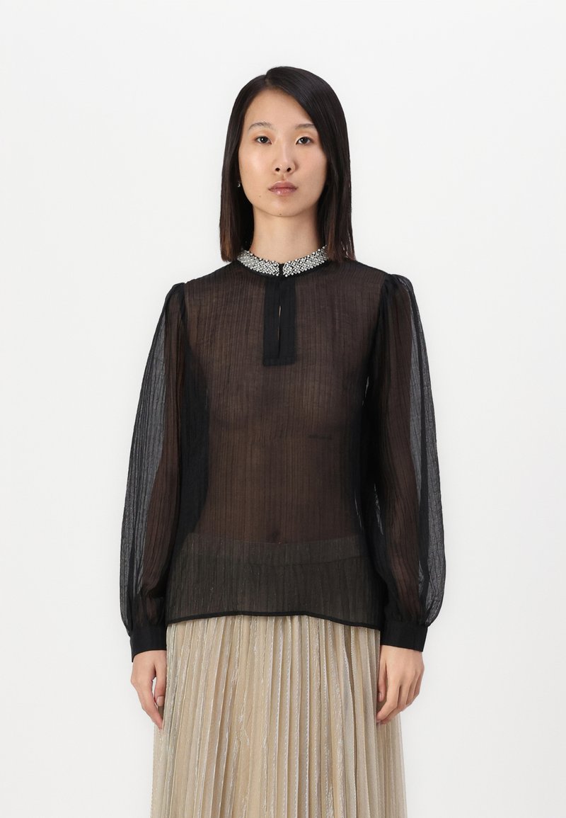 Blusa nera trasparente con lunghe maniche a sbuffo, colletto dettagliato con embellishments e apertura centrale a forma di chiave. Tessuto texture con sottili righe.