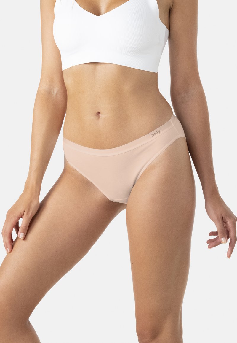 Femme portant un soutien-gorge de sport blanc et une culotte sans coutures beige clair de style bikini, sur un fond uni.