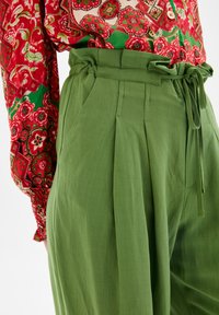 Gröna högmidjade byxor med veck och ett knytbälte, tillverkade av lättviktigt material; matchas med en långärmad blus i rödblommat mönster.