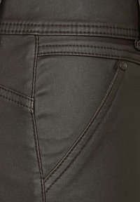 Mörkbrun denimtyg med en rundad fickdesign, synliga sömmar och metallbeslag. Slät textur med en lätt lyster.