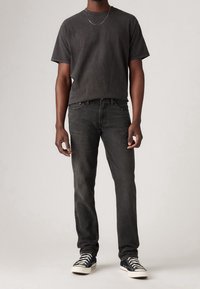 Svart T-shirt med korta ärmar och rund hals, kombinerad med mörkgrå jeans. Accentuerad med ett tunt silverhalsband och svarta sneakers.