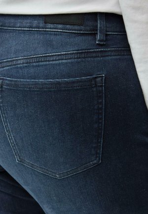 Dark blue denim jeans with a smooth texture, featuring a back pocket with a pointed shape and minimalistic stitching detail.
