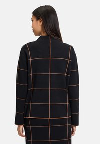 Schwarze Strickjacke mit orangefarbenem Karomuster, runder Halsauschnitt und lockerer Passform. Lange Ärmel reichen bis zum Handgelenk.