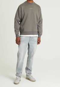 Sweat-shirt en coton gris à épaules tombantes avec un logo blanc, associé à un jean bleu clair et des baskets grises à semelles beiges.