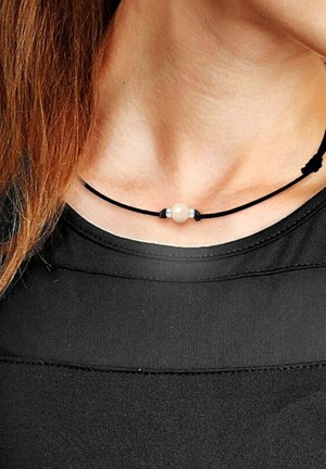 Collier en cordon noir avec une perle centrale lisse de couleur claire, flanquée de petites accents métalliques. Design simple, porté près du cou.