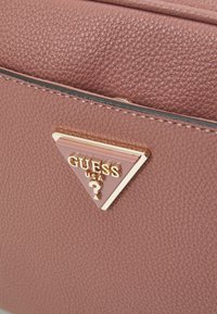 Borsa a tracolla in pelle rosa con un accento triangolare di logo oro e rosa. Presenta cuciture visibili e un design strutturato.
