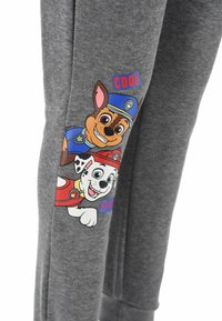 Grijze joggingbroek met cartoonfiguren Chase en Marshall van "Paw Patrol," met kleurrijke tekst "COOL" en "PLAY."