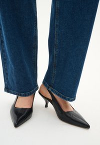 Schwarze Leder-Slingback-Pumps mit spitzem Zehenbereich und einem kleinen, ausgestellten Absatz, kombiniert mit blauen, geraden Denim-Hosen.