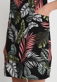 Hand in pocket of black fabric dress with large tropical leaf print in green, white, and coral colors.