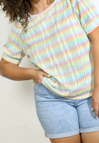 Top de manga corta con un patrón en zigzag en colores pastel sobre una tela ligera, combinado con unos pantalones cortos de mezclilla claros.