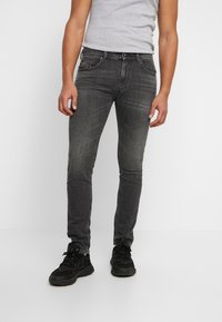 Grey denim jeans with a slim fit silhouette, featuring a classic five-pocket design and subtle fading. Worn with black athletic shoes.
