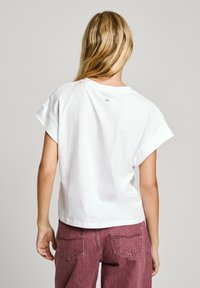 T-shirt blanc à manches courtes avec une coupe décontractée et un petit logo imprimé au dos, associé à un pantalon bordeaux taille haute.