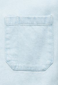 Φωτεινό γαλάζιο υφασμάτινο τζιν με ραμμένη τετράγωνη τσέπη, που διαθέτει γωνιακές κάτω γωνίες και εμφανείς λεπτομέρειες ραφής.