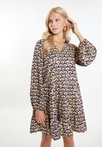 Gėlėmis raštuota suknelė su V formos iškirpte, ilgomis pūstomis rankovėmis ir sluoksniuota apačia. Pagaminta iš lengvos medžiagos, turi tamsiai mėlyną, kremišką ir auksinę spalvas.