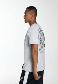 Camiseta de algodón gris con mangas cortas, que presenta una impresión gráfica en la parte posterior. El diseño incluye diversas ilustraciones divertidas.