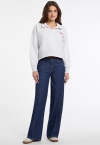 Hellgrauer, taillierter Sweatshirt mit Kragen und roter Stickerei, kombiniert mit dunkelblauen weit geschnittenen Jeans und beigen Sneakers.