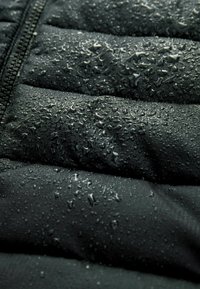 Doudoune noire avec sections matelassées, dotée d'une surface résistante à l'eau ornée de petites gouttelettes. Détail de fermeture zippée visible.