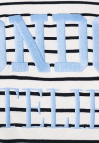 Gebreid textiel met horizontale zwarte en witte strepen en grote lichtblauwe geborduurde letters die "LONDON" en "TELL" spellen.