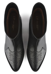 Czarne skórzane botki do kostki z spiczastymi noskami, dekoracyjnym przeszyciem na czubkach oraz gładkim wykończeniem. Wnętrze wykończone brązową podszewką.